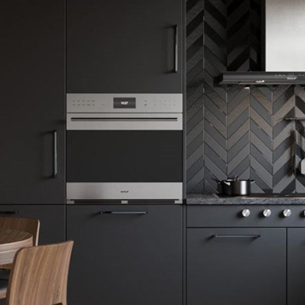 Modern matte-black kitchen with a built-in stainless oven, gas cooktop, and herringbone tile backsplash beneath a slim range hood.